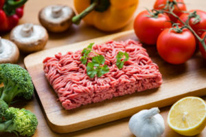 Organic ground beef (minced meat) on a wooden cutting board in the kitchen.